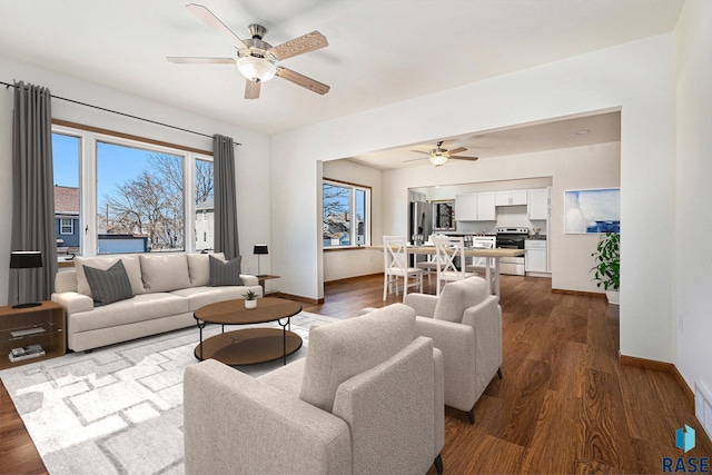 living room with plenty of natural light, ceiling fan, dark wood-type flooring, and baseboards