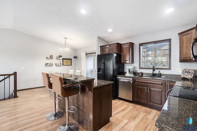 kitchen with a kitchen island, lofted ceiling, a sink, black appliances, and a kitchen breakfast bar