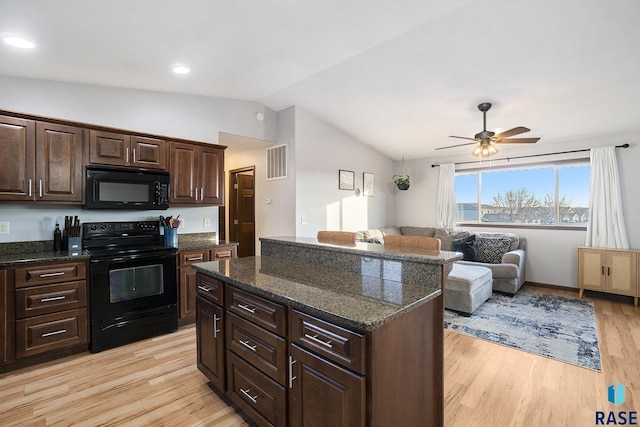 kitchen featuring visible vents, a kitchen island, light wood-style flooring, black appliances, and vaulted ceiling