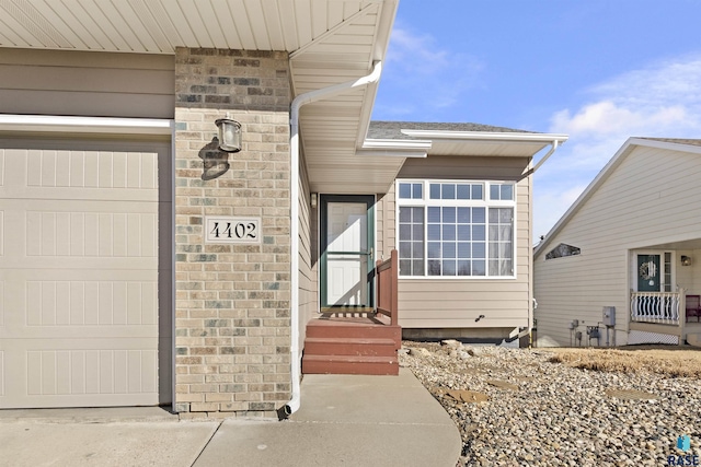 view of exterior entry featuring brick siding, a shingled roof, and a garage