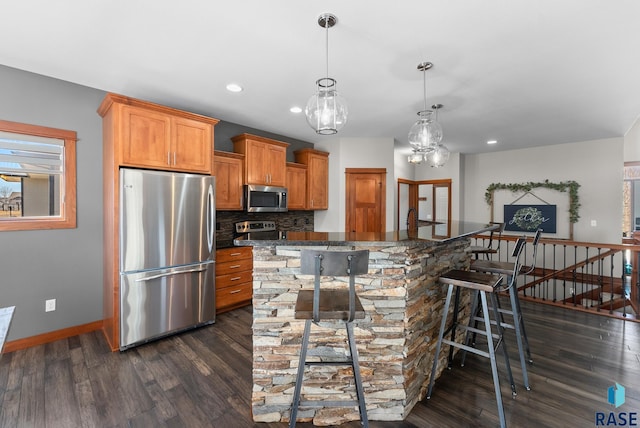 kitchen with baseboards, dark wood-type flooring, appliances with stainless steel finishes, a kitchen breakfast bar, and backsplash