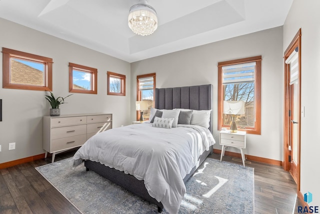 bedroom with a raised ceiling, a notable chandelier, multiple windows, and baseboards