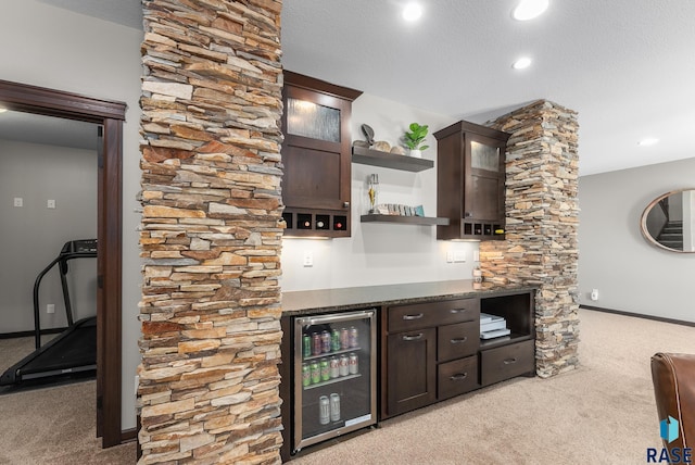 bar with beverage cooler, a textured ceiling, a bar, baseboards, and light colored carpet