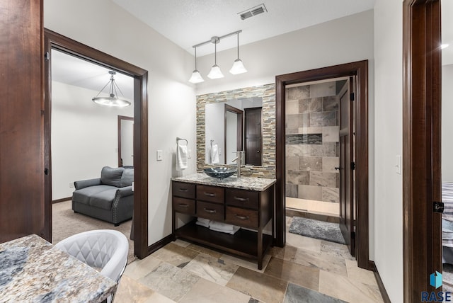 full bathroom with a tile shower, visible vents, vanity, and baseboards