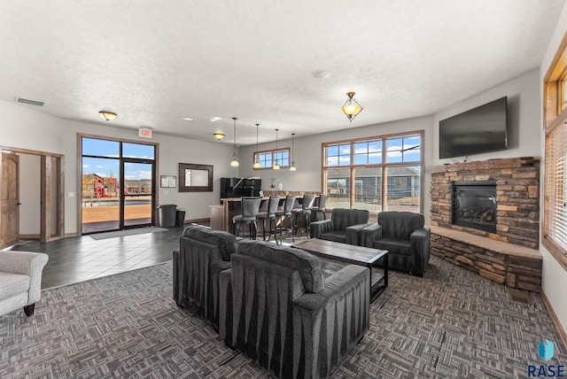 living room featuring visible vents, baseboards, a fireplace, a textured ceiling, and dark tile patterned flooring