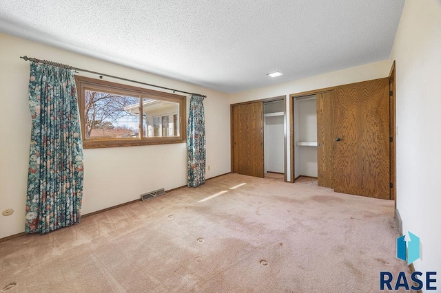 unfurnished bedroom with visible vents, carpet floors, two closets, and a textured ceiling