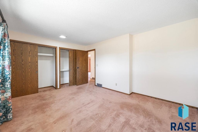 unfurnished bedroom featuring visible vents, multiple closets, a textured ceiling, carpet, and baseboards