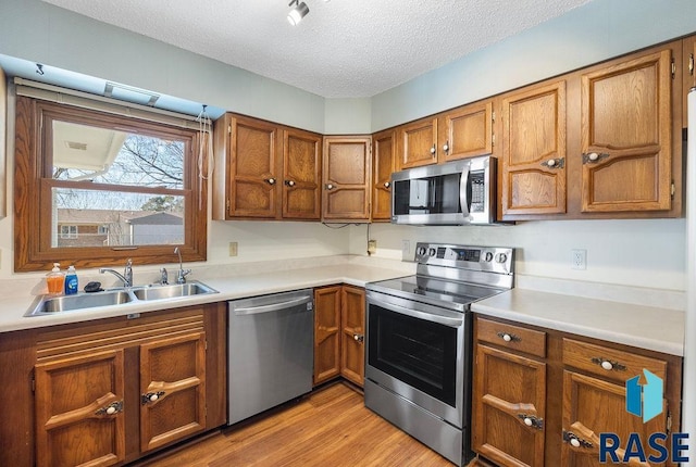 kitchen featuring brown cabinetry, light wood-style flooring, a sink, stainless steel appliances, and a textured ceiling