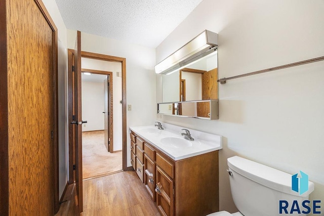 bathroom with a sink, toilet, double vanity, and a textured ceiling