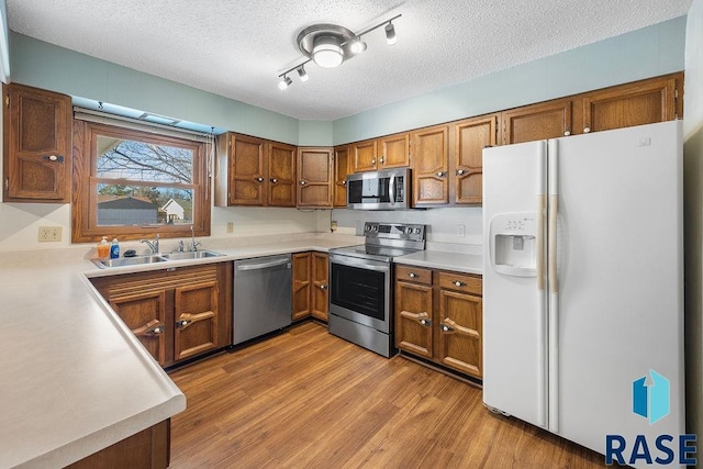 kitchen featuring brown cabinets, stainless steel appliances, light wood-style floors, and a sink