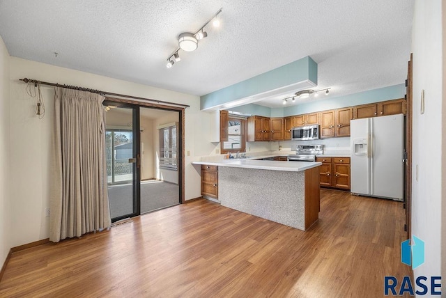 kitchen featuring a peninsula, a sink, stainless steel appliances, light countertops, and brown cabinets