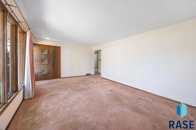 unfurnished room featuring a textured ceiling, baseboards, visible vents, and light carpet