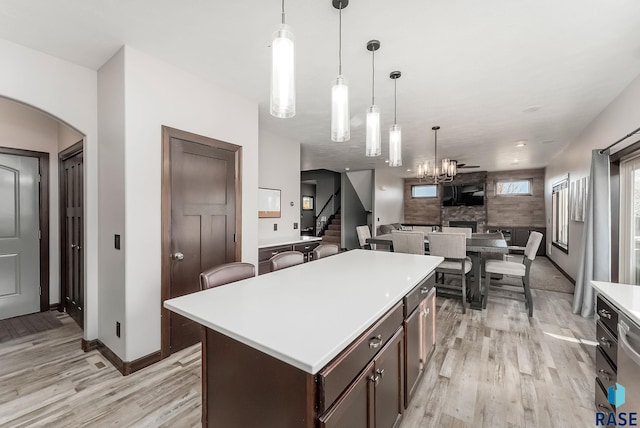 kitchen with a center island, light wood-style floors, a stone fireplace, light countertops, and dark brown cabinets