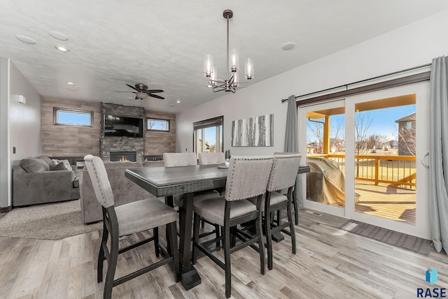 dining room with light wood-style flooring, recessed lighting, a fireplace, a textured ceiling, and ceiling fan with notable chandelier