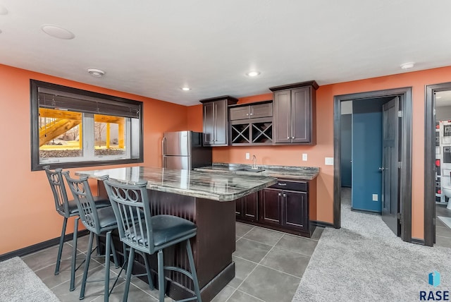 kitchen featuring a kitchen bar, a center island, freestanding refrigerator, stone counters, and baseboards