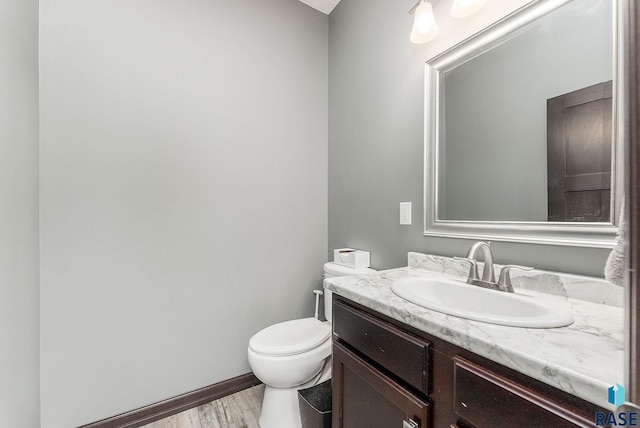 half bath featuring vanity, toilet, wood finished floors, and baseboards