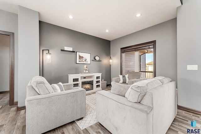 living room with visible vents, a glass covered fireplace, recessed lighting, light wood-style floors, and baseboards