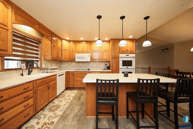 kitchen featuring white appliances, brown cabinetry, a kitchen island, and a sink