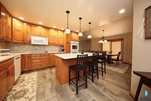 kitchen with backsplash, white appliances, a breakfast bar area, and brown cabinets