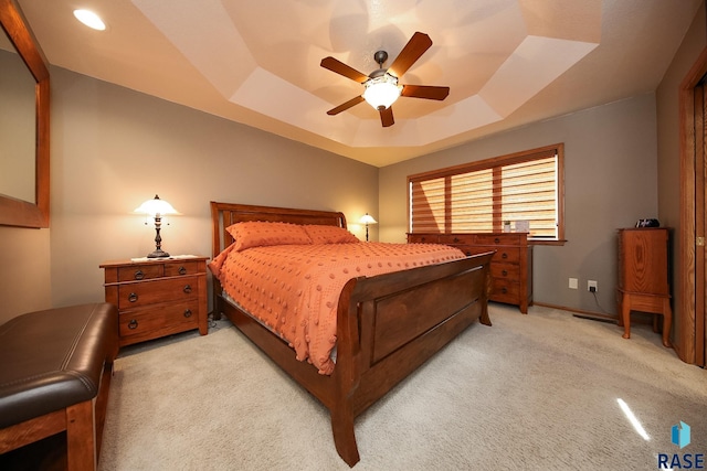 bedroom featuring ceiling fan, a tray ceiling, baseboards, and light carpet