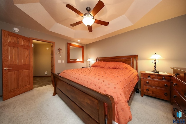 bedroom featuring a tray ceiling, light colored carpet, and ceiling fan