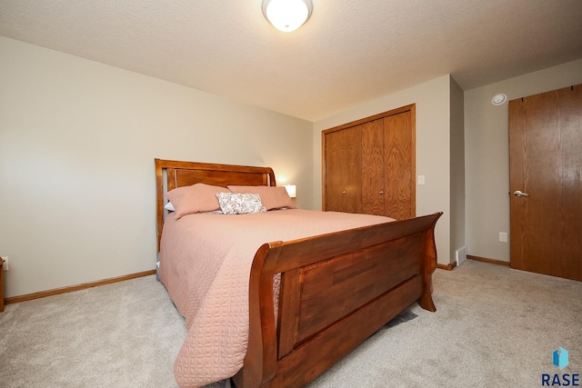 bedroom with a closet, light colored carpet, a textured ceiling, and baseboards