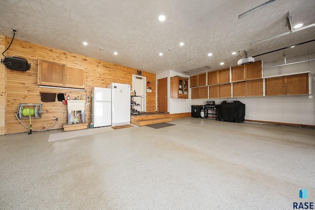 garage with wooden walls, recessed lighting, a garage door opener, and freestanding refrigerator