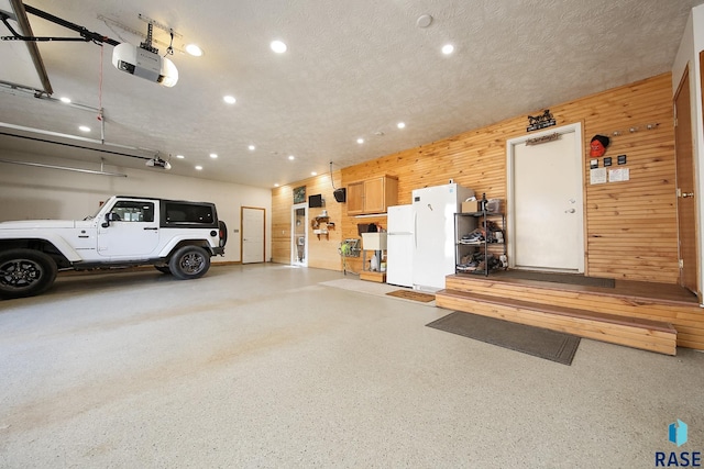 garage with freestanding refrigerator, recessed lighting, a garage door opener, and wood walls