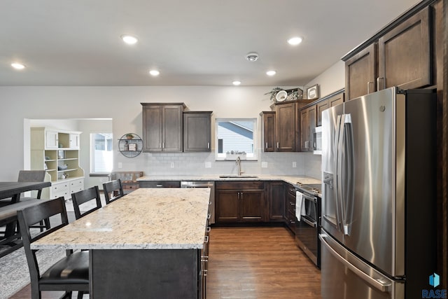 kitchen featuring dark wood-type flooring, a sink, a center island, dark brown cabinetry, and appliances with stainless steel finishes