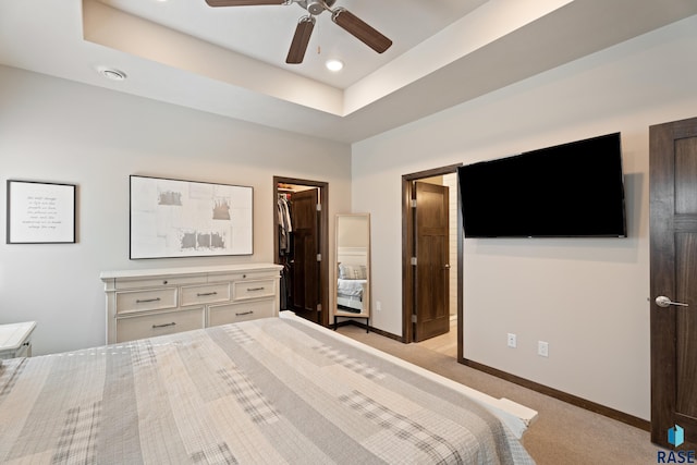 bedroom featuring a spacious closet, baseboards, light colored carpet, a raised ceiling, and a ceiling fan