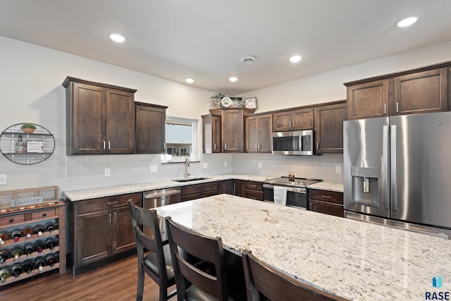 kitchen with a sink, light stone counters, dark wood-style floors, dark brown cabinetry, and appliances with stainless steel finishes