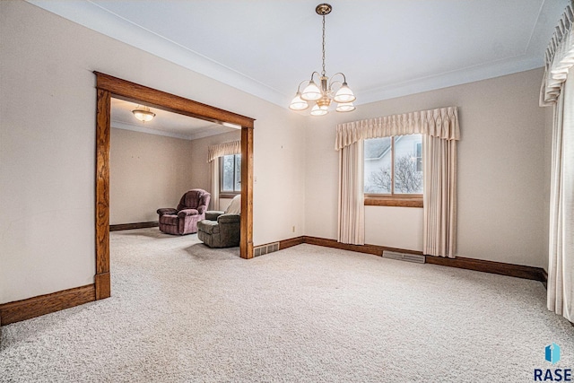 carpeted spare room featuring a wealth of natural light, visible vents, a notable chandelier, and ornamental molding