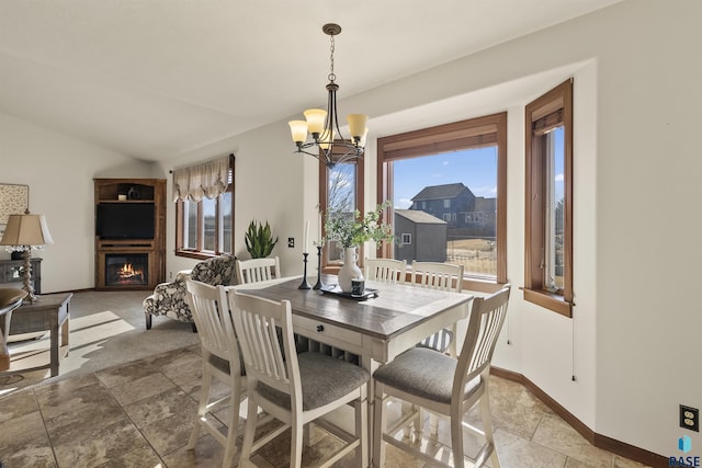 dining space featuring an inviting chandelier, vaulted ceiling, a fireplace, and baseboards