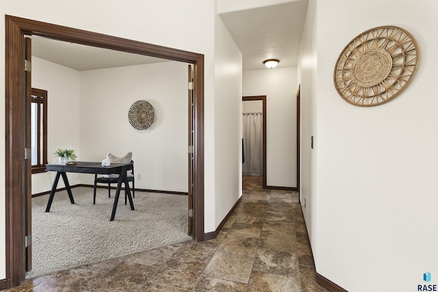 hallway with stone finish floor, baseboards, and dark colored carpet