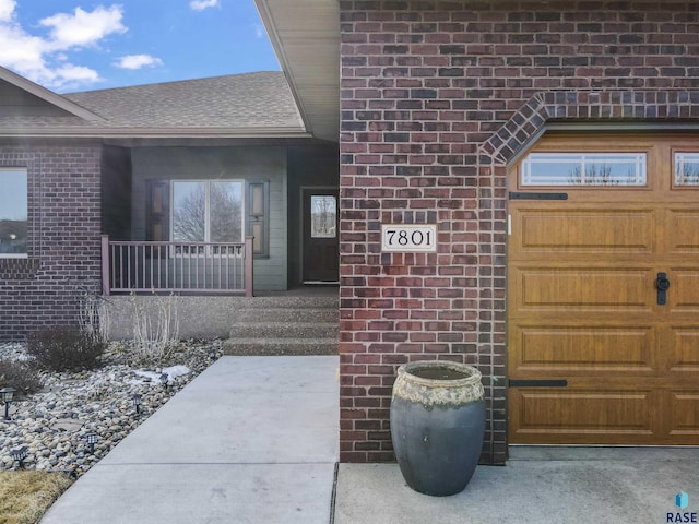 property entrance featuring covered porch, brick siding, and roof with shingles