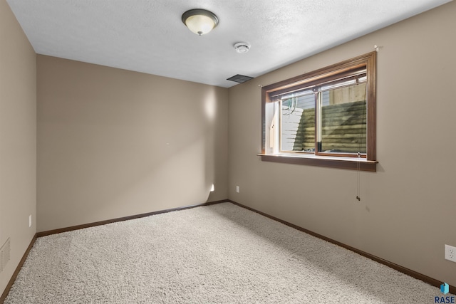 carpeted spare room featuring a textured ceiling and baseboards