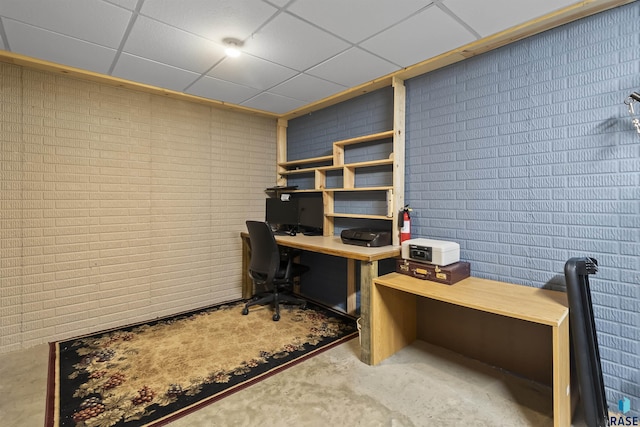 office with a paneled ceiling, brick wall, and unfinished concrete floors