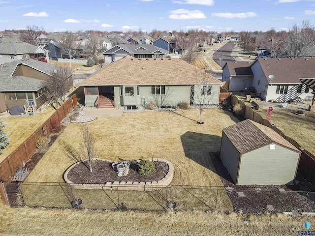 rear view of house featuring a fenced backyard, an outdoor structure, a storage shed, a lawn, and a residential view