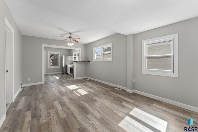 unfurnished living room with visible vents, wood finished floors, baseboards, and ceiling fan