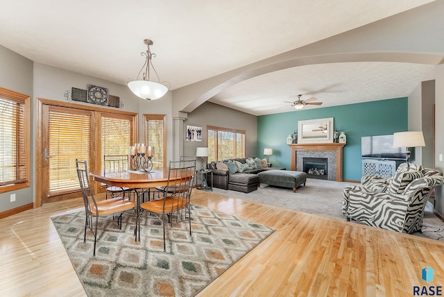 dining space with baseboards, arched walkways, wood finished floors, and a tile fireplace