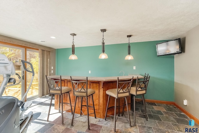 bar with stone finish flooring, a textured ceiling, wet bar, baseboards, and hanging light fixtures