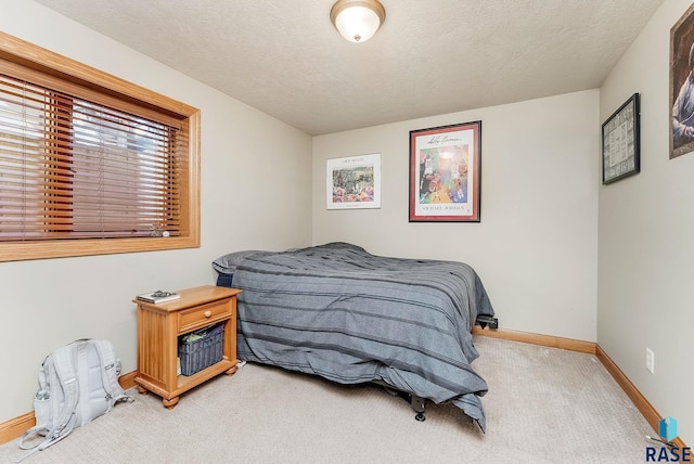 bedroom featuring baseboards, light carpet, and a textured ceiling