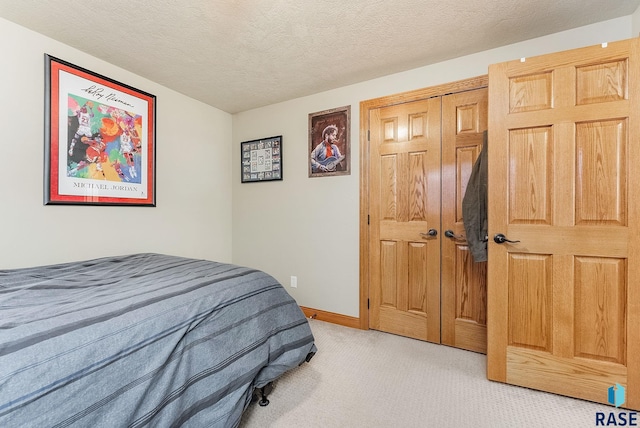 bedroom featuring light colored carpet, baseboards, a closet, and a textured ceiling