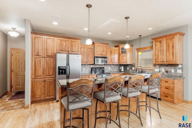 kitchen featuring appliances with stainless steel finishes, a kitchen island, light wood-type flooring, and a sink