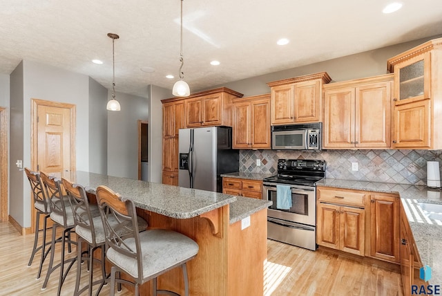 kitchen featuring light wood-type flooring, backsplash, a kitchen island, appliances with stainless steel finishes, and light stone countertops