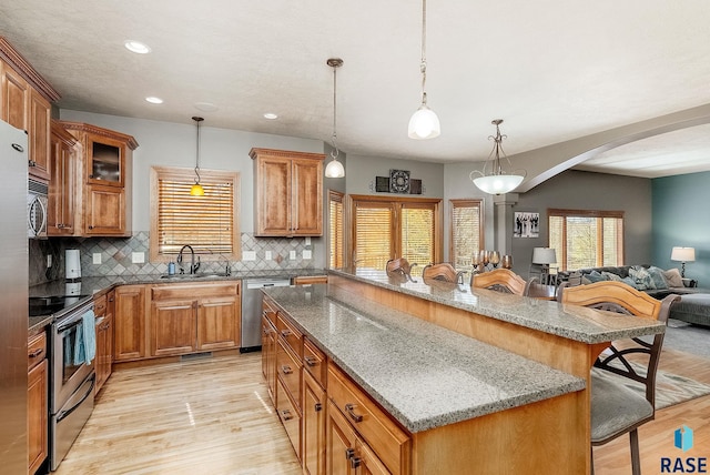 kitchen featuring a kitchen island, a breakfast bar area, appliances with stainless steel finishes, arched walkways, and a sink