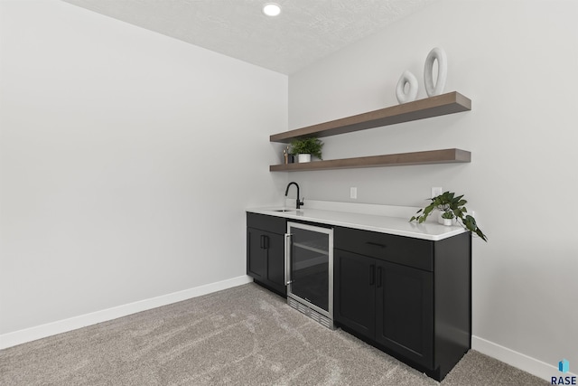 bar featuring a textured ceiling, wine cooler, indoor wet bar, baseboards, and light colored carpet