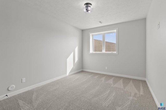 spare room with light carpet, visible vents, a textured ceiling, and baseboards