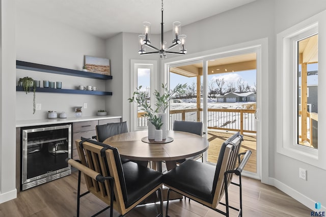 dining space with beverage cooler, a notable chandelier, baseboards, and wood finished floors