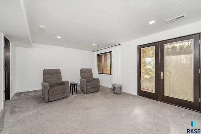 living area featuring visible vents, baseboards, carpet, and a textured ceiling